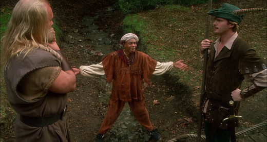 Don't Riyadh into it too much. A scene from Robin Hood: Men In Tights showing Ahchoo (Dave Chappelle) straddling a small stream, framed slightly below a small bridge and by Robin of Loxley (Cary Elwes) and Little John (Eric Allan Kramer).